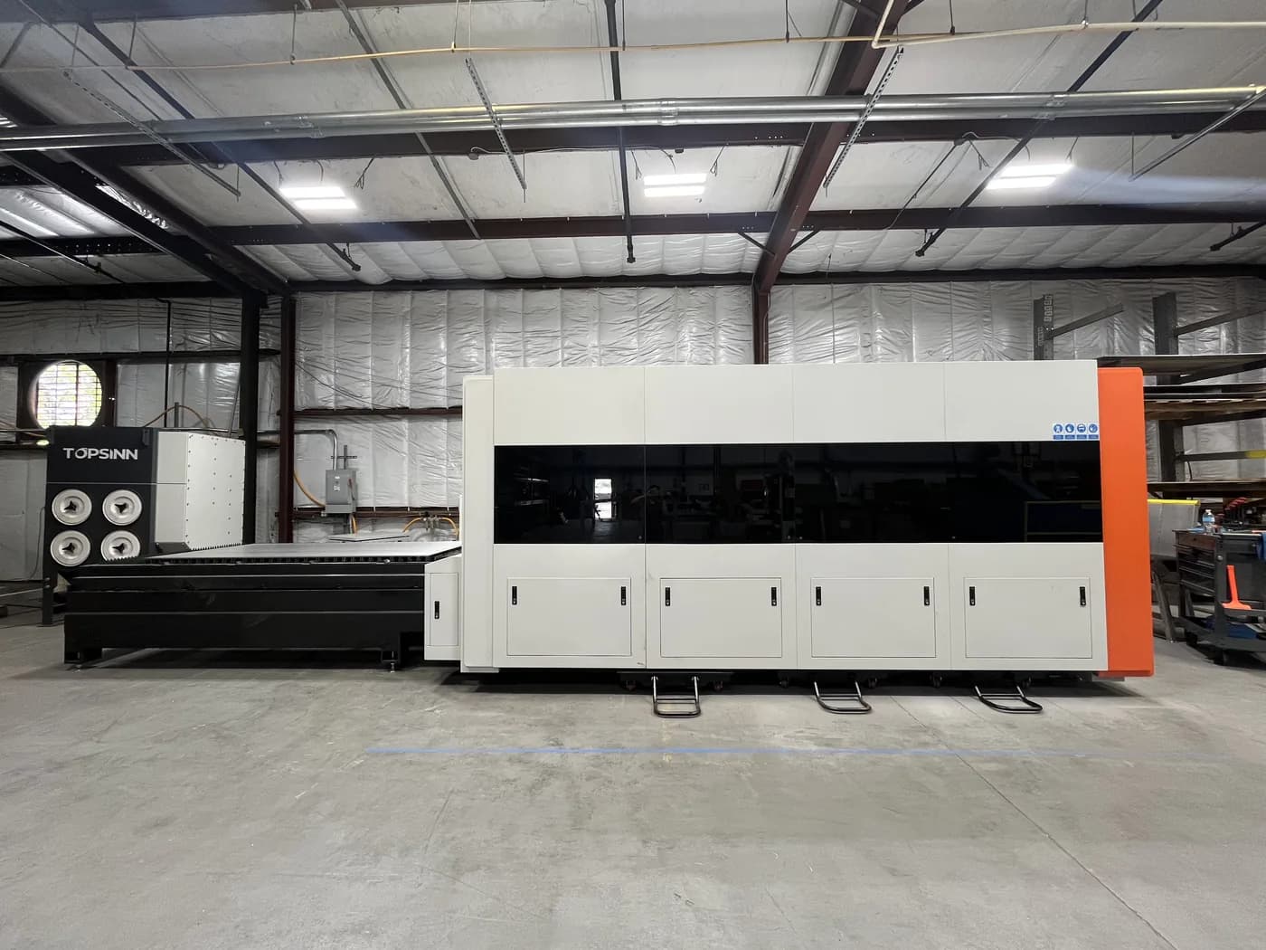 Enclosed fiber laser cutting machine with its flat sheet table on the shop floor.